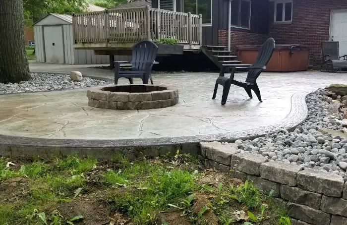 A backyard stamped concrete patio with patio chairs table and fire pit