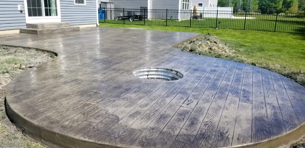 Outdoor brownish Stamped Concrete patio with sunken fire pit in the center of it.